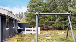 A house with a deck, a swing set, and a white picket fence.
