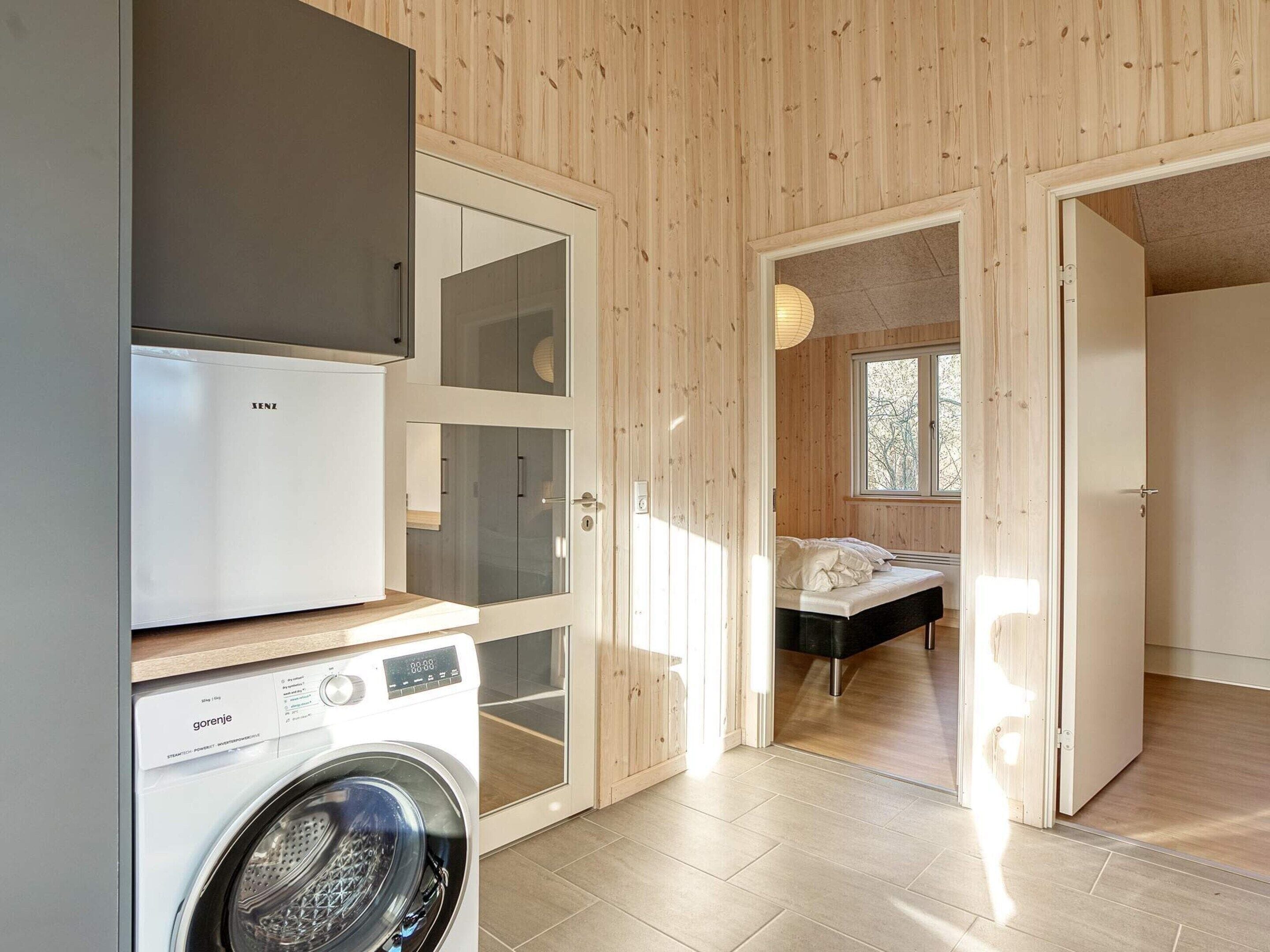 Ein kleines Zimmer mit Waschmaschine, Bett und Fenster.