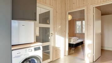 Ein kleines Zimmer mit Waschmaschine, Bett und Fenster.