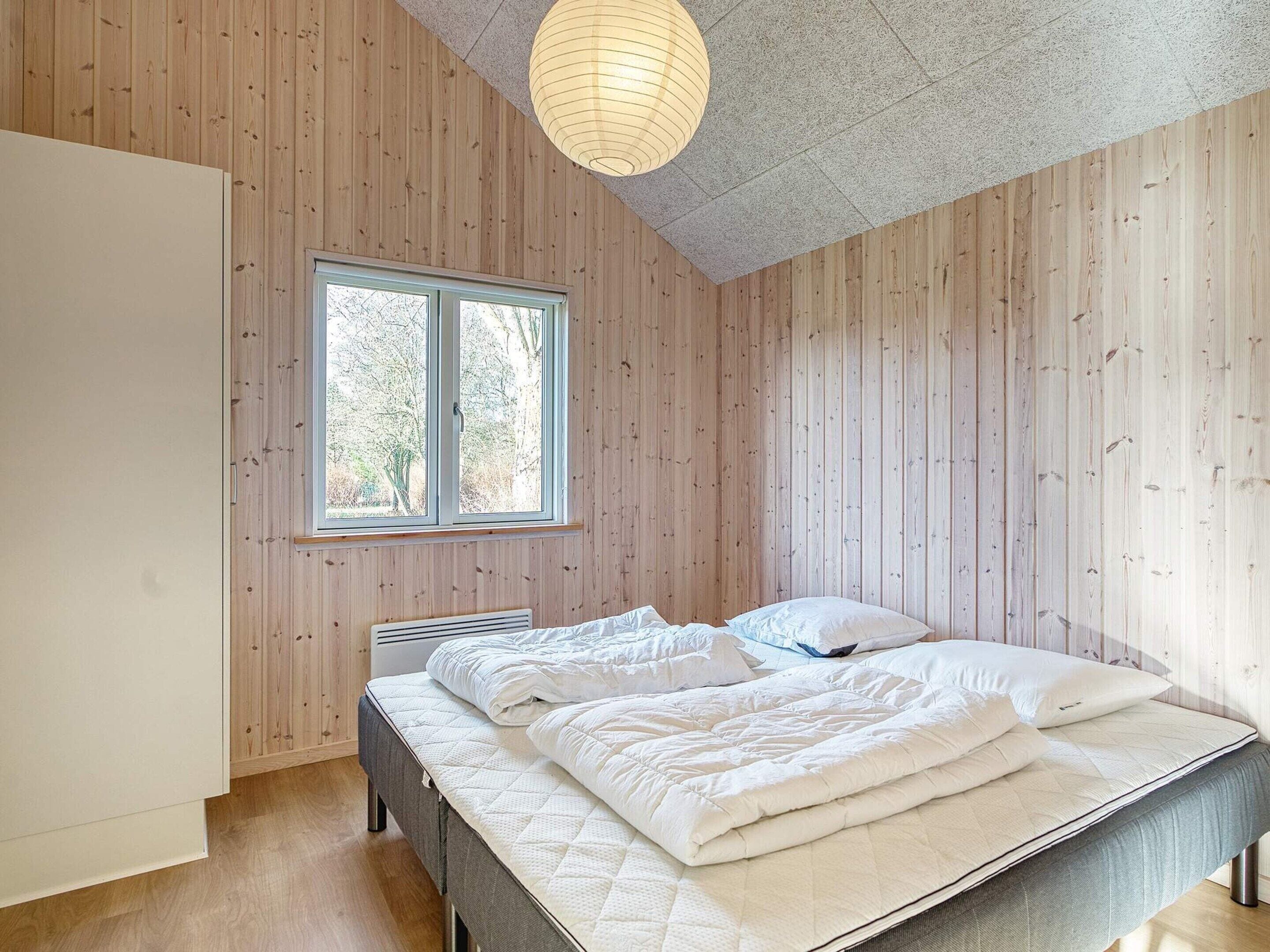 A bedroom with a bed, a window, and wooden walls.