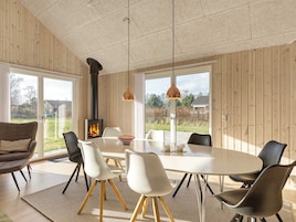 A modern interior with a round dining table, white chairs, a wood-paneled wall, and a visible fireplace.