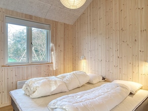 A room with wooden panel walls, a bed with white bedding, a window with a view of trees, and a wall-mounted light fixture. - 8 Person Holiday Home in Dannemare (Dannemare)