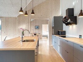 A modern kitchen with wooden cabinetry, a central island with a sink, pendant lighting, and a view into the dining area.