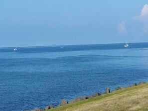 Blick auf die Küste mit ruhigem Meer, felsigem Ufer und Booten in der Ferne.