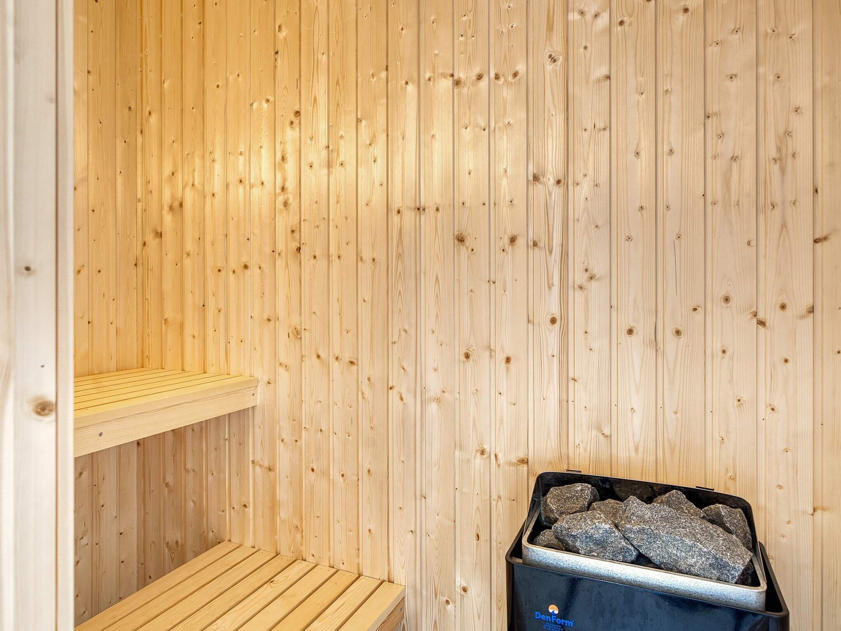 A sauna room with wooden walls, a bench, and a container of stones.
