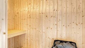 Ein Saunaraum mit Holzwänden, einer Sitzbank und einem Behälter mit Steinen.