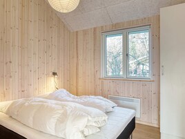 A bedroom with wooden panel walls, a bed with white bedding, a window with a view of trees, and a ceiling light fixture.