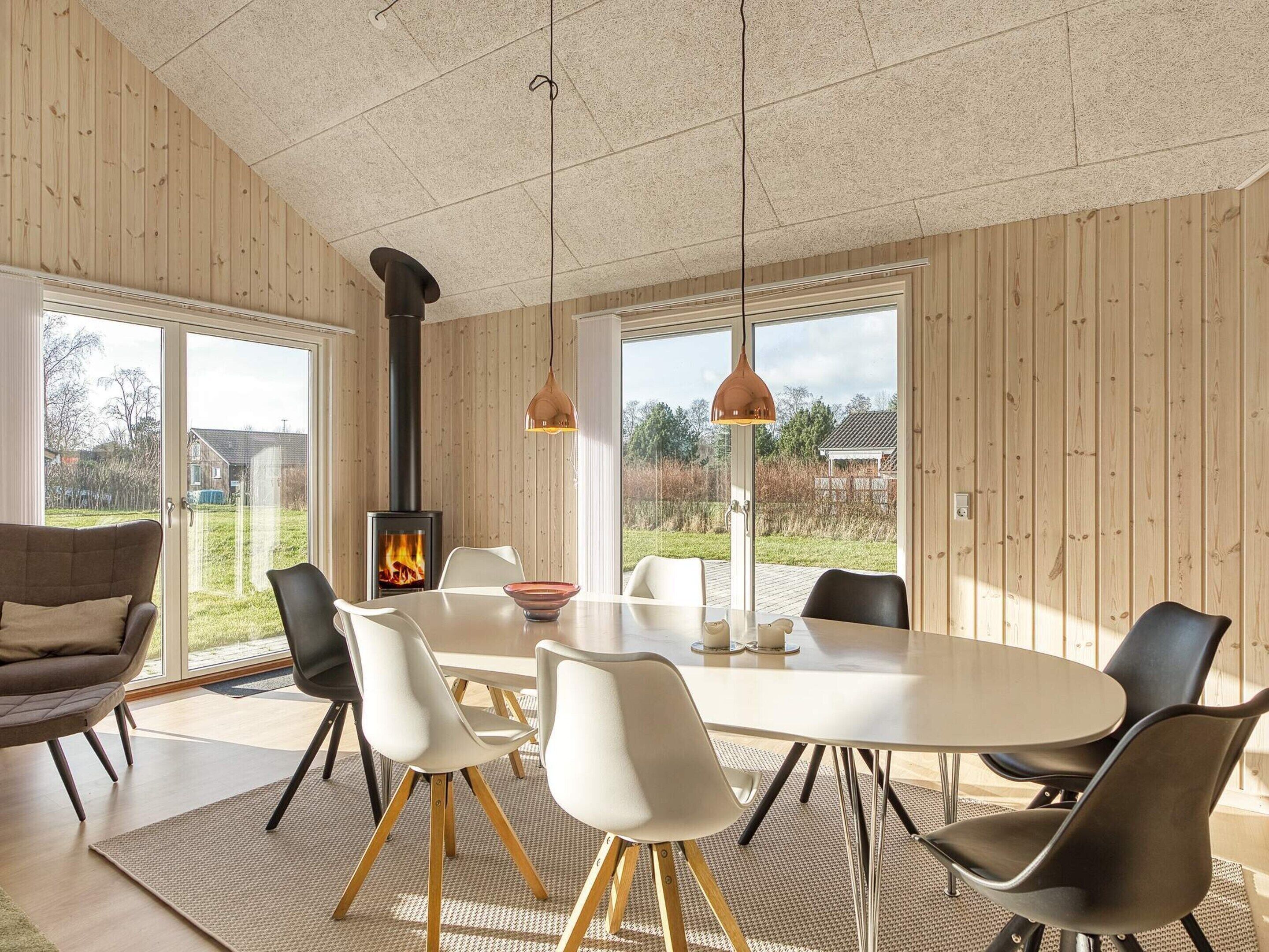 Un interior moderno con una mesa de comedor redonda, sillas blancas, un revestimiento de madera y una chimenea visible.