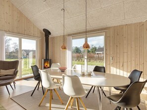 A modern interior with a round dining table, white chairs, a wood-paneled wall, and a visible fireplace. - 8 Person Holiday Home in Dannemare (Dannemare)