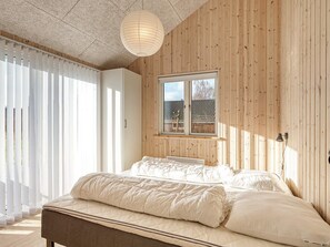 A bedroom with a bed, a window, and wooden walls.