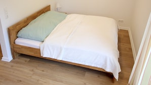 Un lit simple avec un cadre en bois, un matelas blanc et un oreiller vert.