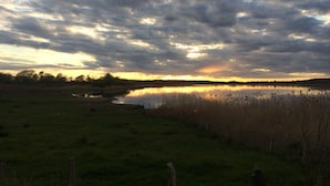 Un paysage paisible, avec une étendue d’eau qui reflète le ciel, entourée de prairies verdoyantes et d’une clôture.
