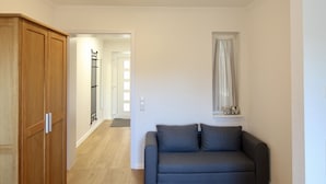 Une pièce avec une armoire en bois, un canapé gris et une fenêtre avec des rideaux.
