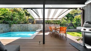 Ein Garten mit Schwimmbad, Sitzgelegenheit und Grill.