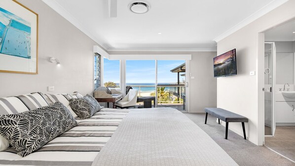 Un dormitorio moderno con una cama grande, un sofá, un televisor y un balcón con vista al mar.