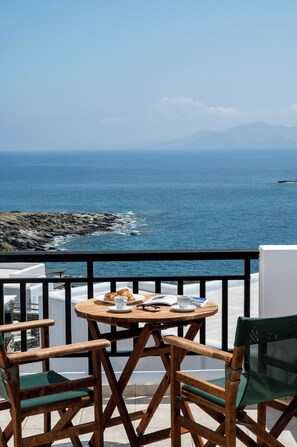 Uma varanda com mesa e cadeiras de madeira, com vista para a costa rochosa e o mar.