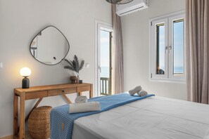 A hotel room with a bed, a wooden desk, a mirror, a lamp, a window with curtains, and a balcony view.