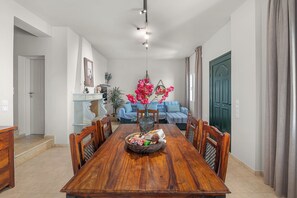 A dining area with a wooden table, chairs, a vase with flowers, and a blue sofa in the background.