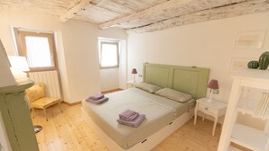 Une chambre avec un plancher en bois, un lit doté d’une tête de lit verte, deux tables de chevet avec des lampes, une chaise et un radiateur.