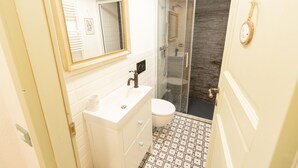 Une salle de bain avec un meuble-lavabo blanc, un miroir avec un cadre doré, des toilettes et une cabine de douche en verre.