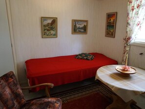 A room with a red bed, a small table with a floral centerpiece, and two framed paintings on the wall. - 5 Person Holiday Home in Mullhyttan (Mullhyttan)