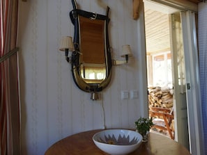 A room with a wooden-framed mirror, two wall-mounted lamps, a white ceramic bowl with a floral design, and a small potted plant. - 5 Person Holiday Home in Mullhyttan (Mullhyttan)