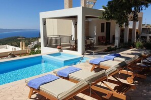 A pool area with lounge chairs and a view of the sea. - Hara House in Monolithos Rhodes (Rhodes)