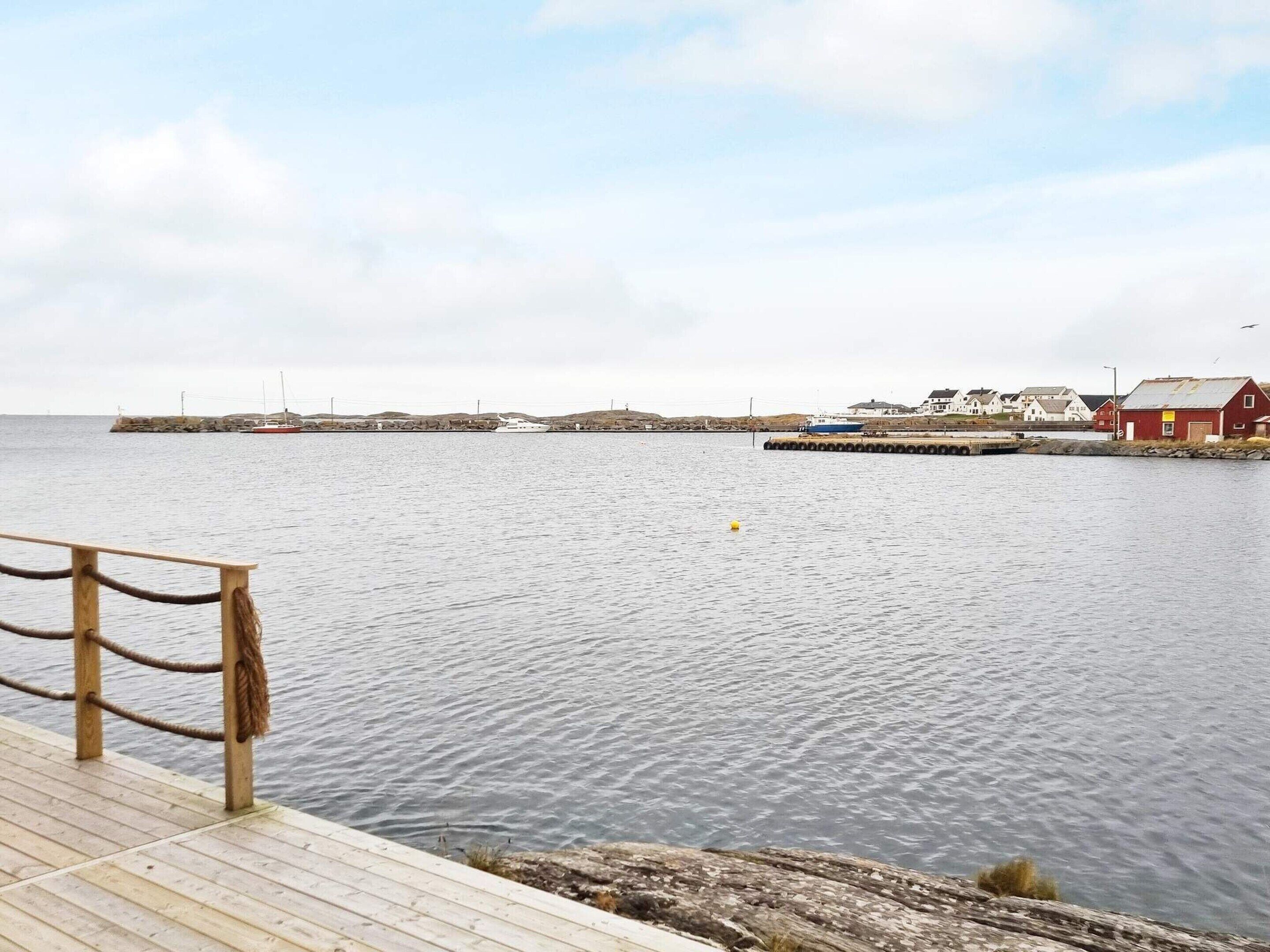A wooden pier extending into calm waters with a red building on the right and a white building in the background.