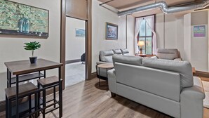 Un salon moderne avec un canapé gris, une petite table ronde, une table basse en bois et un tableau accroché au mur.