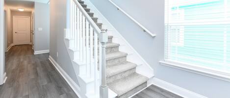 A staircase with white railings and carpeted steps, leading to a room with a door and a window with blinds.