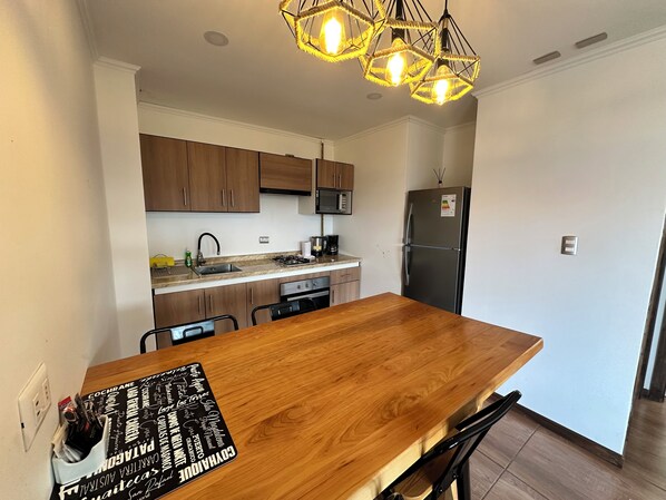 A modern kitchen with wooden cabinets, a stainless steel refrigerator, and a wooden dining table.