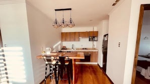 A modern kitchen with wooden cabinets, a central island, and a hanging light fixture. - Alto Balmaceda Apartamentos (Natales)