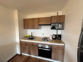 Cocina compacta con muebles de madera, microondas integrado, estufa a gas, cafetera y lavavajillas.