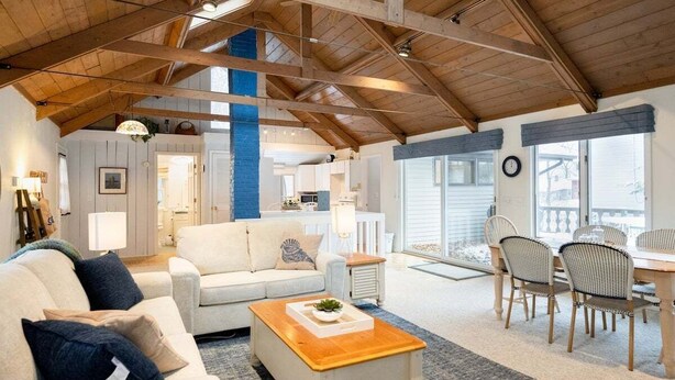 A spacious living area with a high ceiling, wooden beams, a sofa, a coffee table, and a dining area with chairs and a table. - Updated cottages steps from Lake Michigan beach (West Olive)