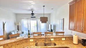 A kitchen with granite countertops, wooden cabinets, a built-in dishwasher, and a large window with a view of the outdoors. - Second Row Condo with Ocean Views, Pool, and Hot tub (Oak Island)