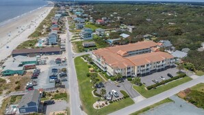 An aerial view of a coastal residential area with a beach, houses, and a large building with a red roof. - Second Row Condo with Ocean Views, Pool, and Hot tub (Oak Island)