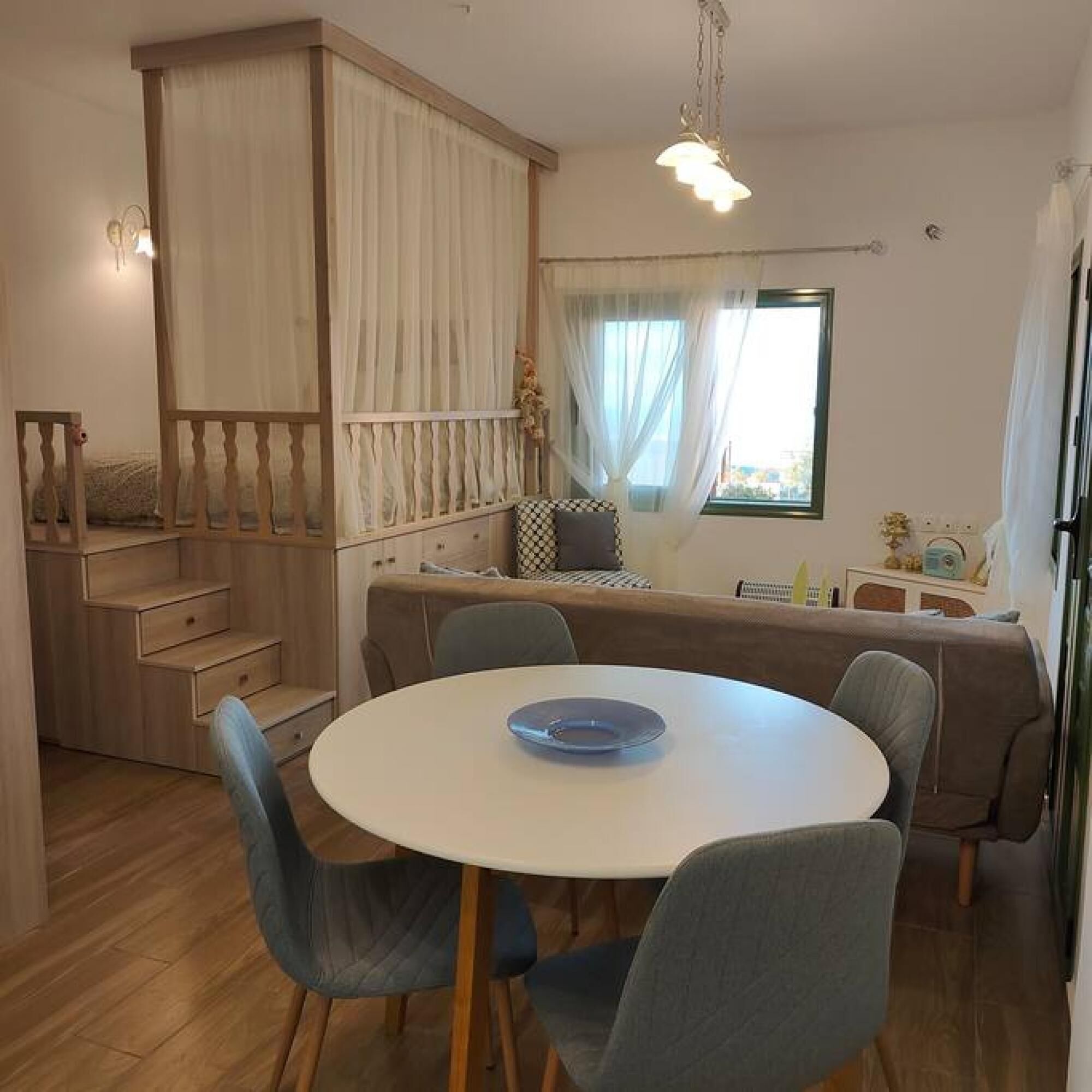 A dining area with a round table, blue chairs, a wooden cabinet, and a window with curtains.