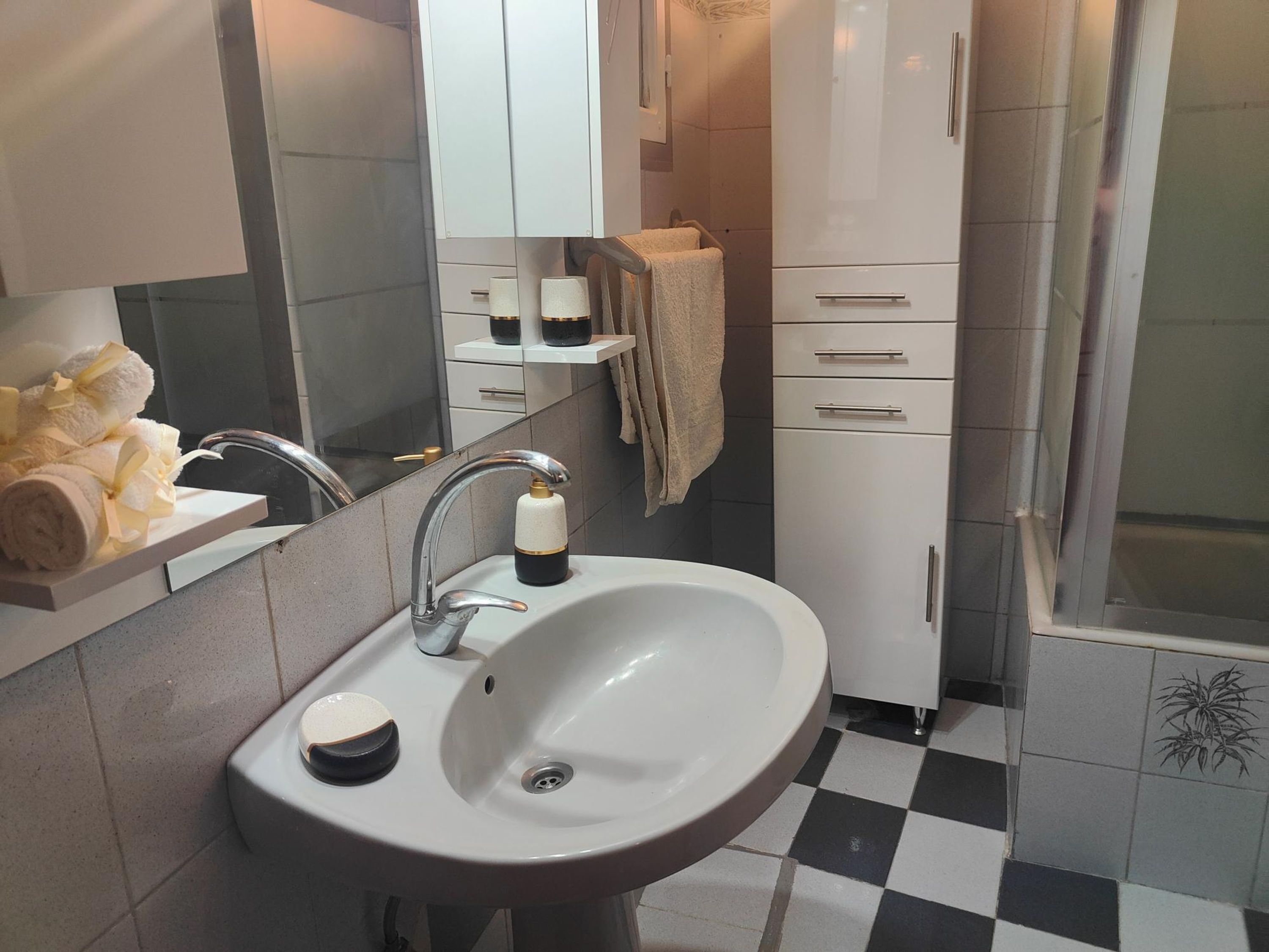 Un bagno con un lavandino bianco, uno specchio, un portasciugamani e uno spazio doccia.
