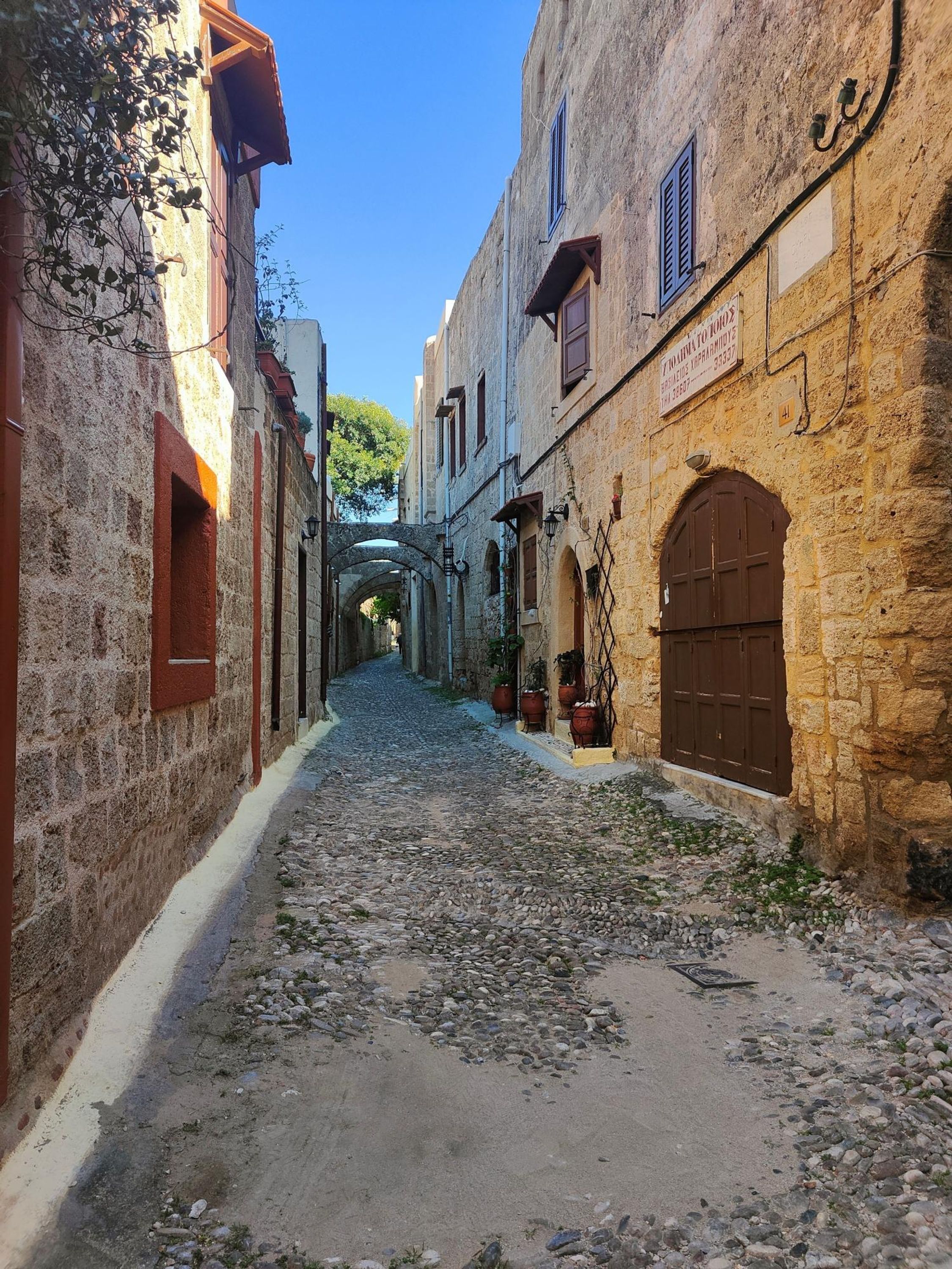 Una stretta strada acciottolata, fiancheggiata da edifici storici in pietra con portali ad arco e persiane.