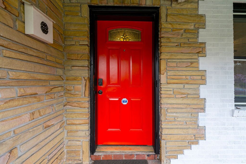 A red door with a brass knocker, a mailbox, and a small window to the right.