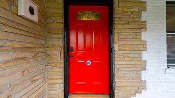 A red door with a brass knocker, a mailbox, and a small window to the right.