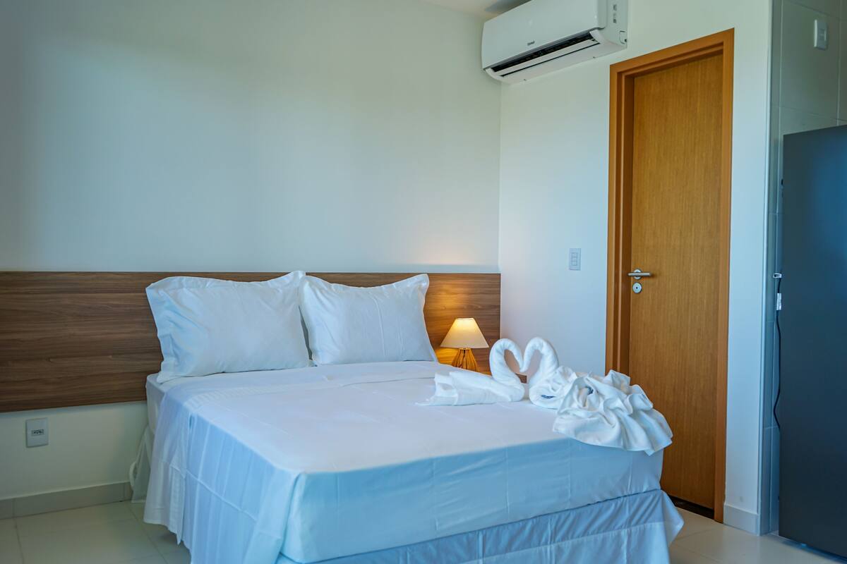 Habitación de hotel con cama, cabecero de madera, unidad de aire acondicionado, puerta y lámpara.