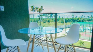 A modern room with a glass table and white chairs, a view of palm trees and a parking lot through large windows. - Mana Beach By Mai (Ipojuca)