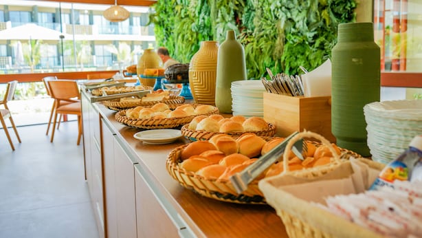 A buffet setup with various food items and utensils, a green wall, and a view of the outdoors. - Mana Beach By Mai (Ipojuca)