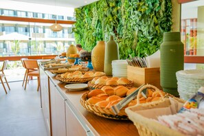 A buffet setup with various food items and utensils, a green wall, and a view of the outdoors.
