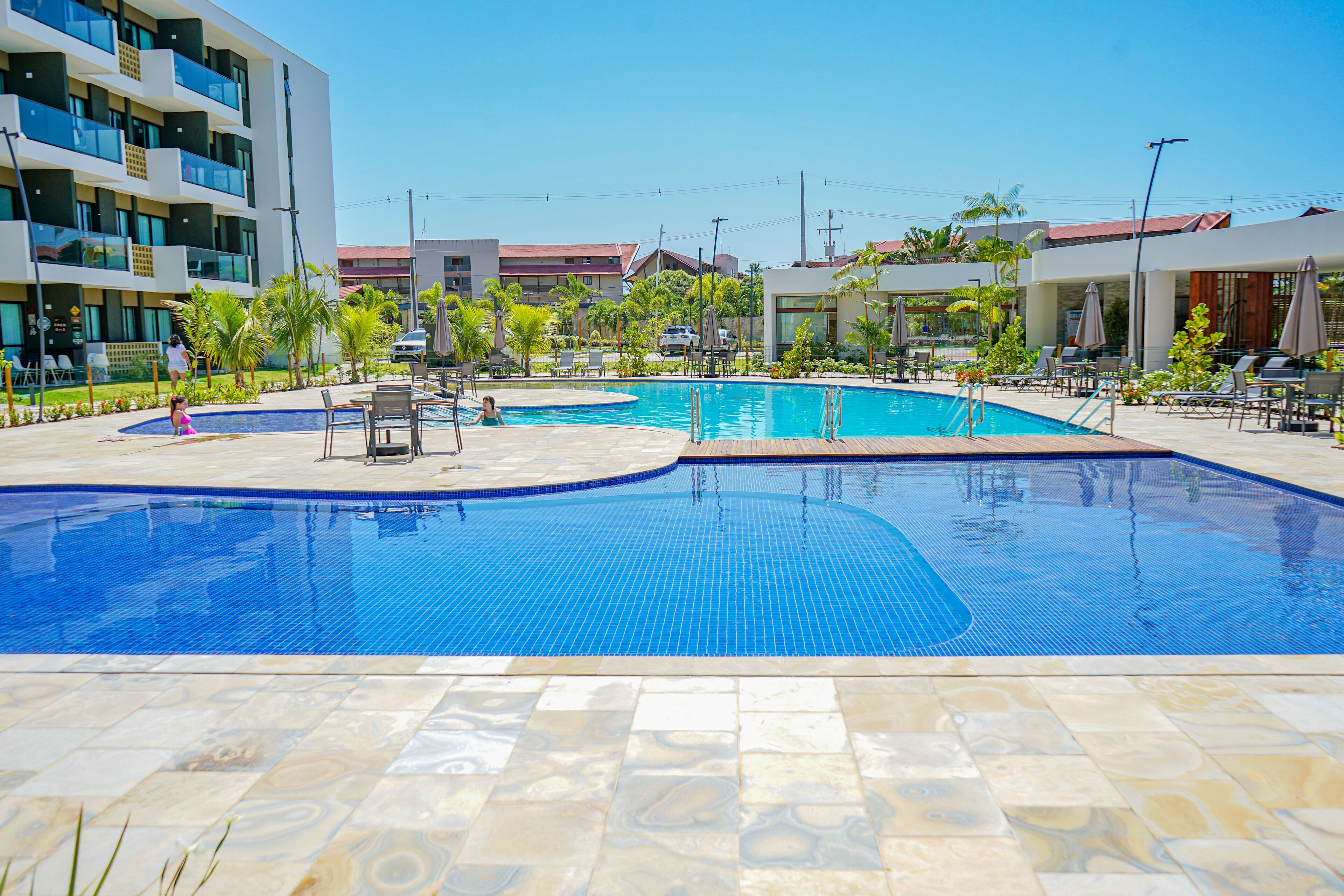 A swimming pool with tiled flooring and lounge chairs around it.
