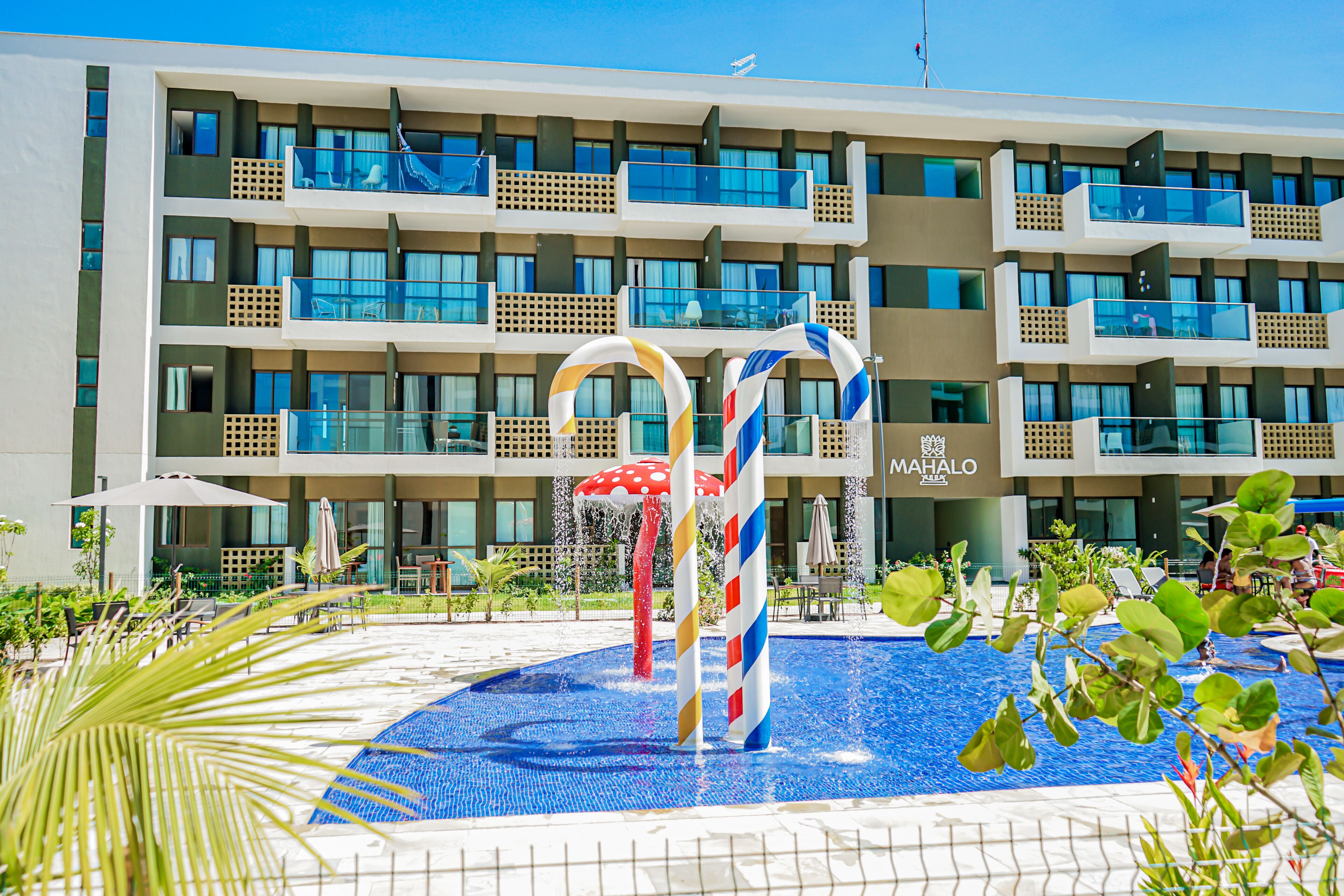 Un hotel con varios balcones, una piscina con fuentes de agua y un cartel que dice "MAHALO".