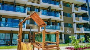 A multi-story hotel with balconies, a wooden play structure, and a well-maintained garden. - Mana Beach By Mai (Ipojuca)