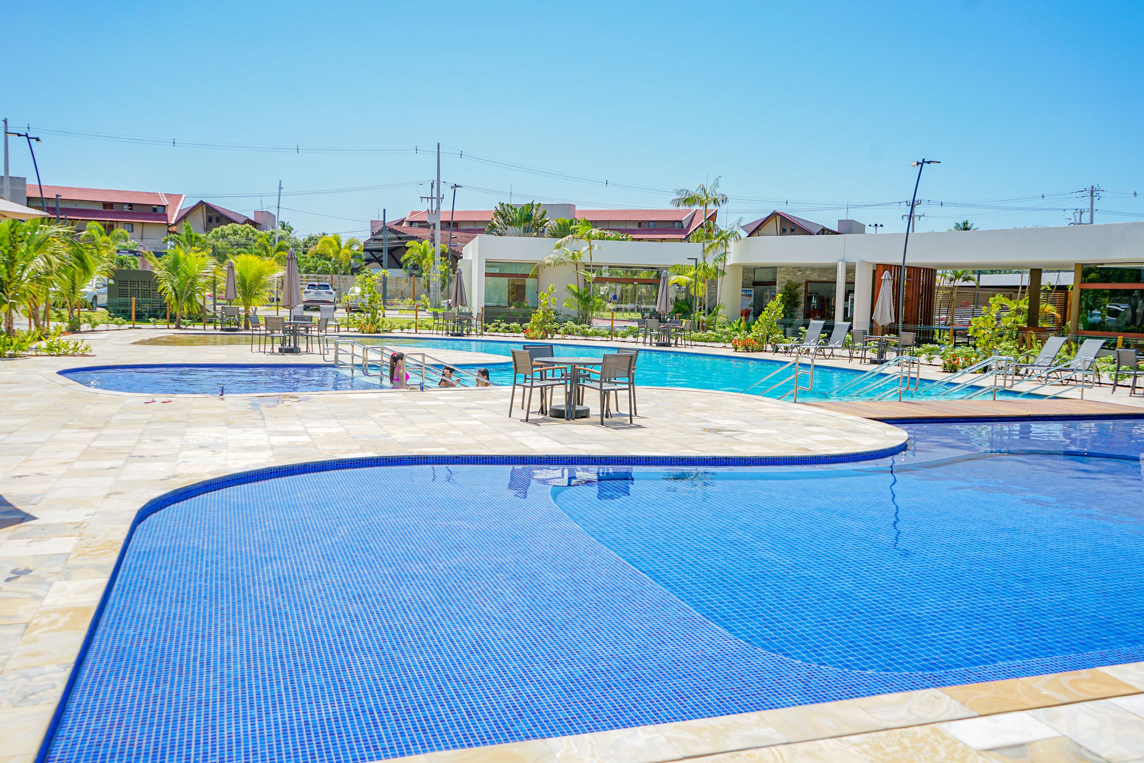A swimming pool area with multiple pools, lounge chairs, and a covered seating area.
