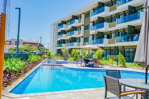 A swimming pool with lounge chairs and umbrellas, surrounded by a multi-story building with balconies. - Mana Beach By Mai (Ipojuca)